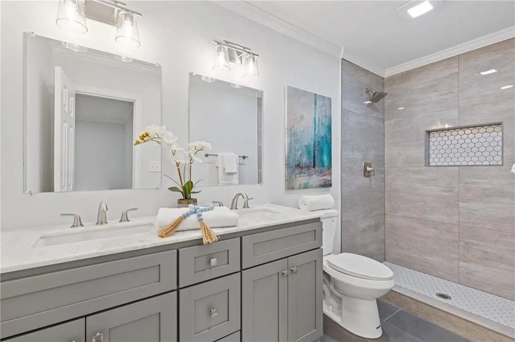 Full bathroom featuring ornamental molding, double vanity, tiled shower, and tile patterned flooring