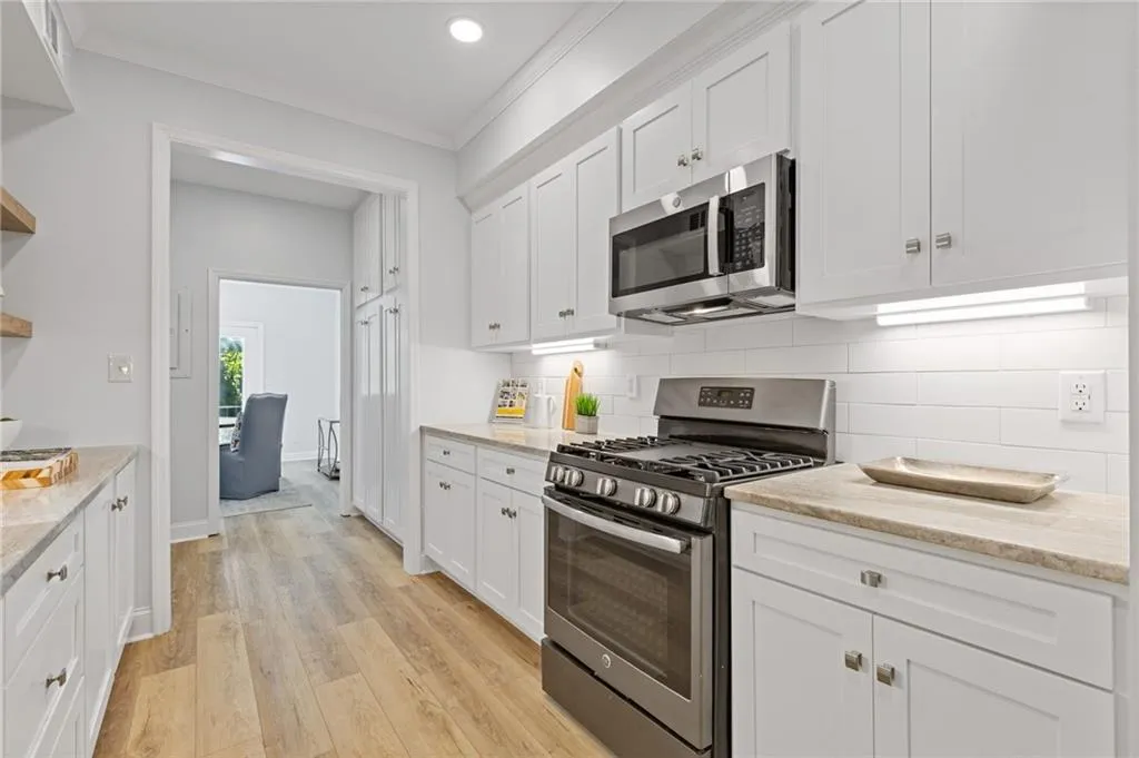 Kitchen with stainless steel appliances, light wood-style floors, crown molding, white cabinets, and light stone countertops