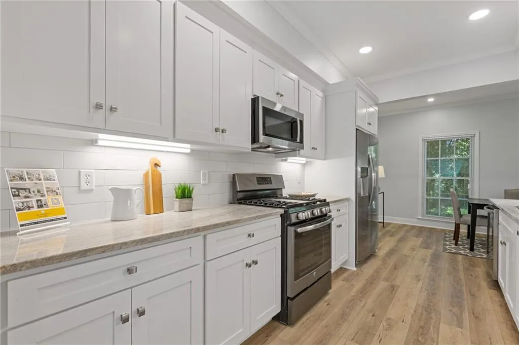 Kitchen with crown molding, stainless steel appliances, light wood-style flooring, white cabinets, and light stone counters
