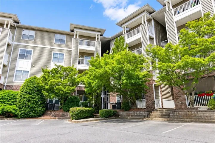 Multi-level condominium building featuring horizontal siding, brick accents, and white balustraded balconies