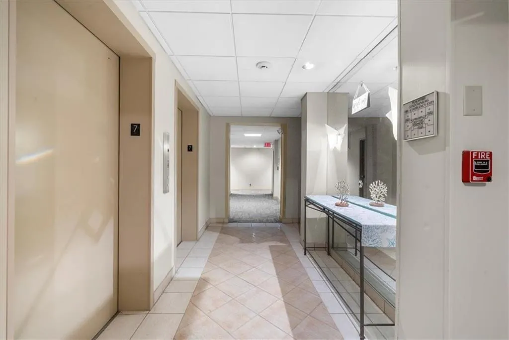 Corridor with a drop ceiling, elevator, and light tile patterned floors