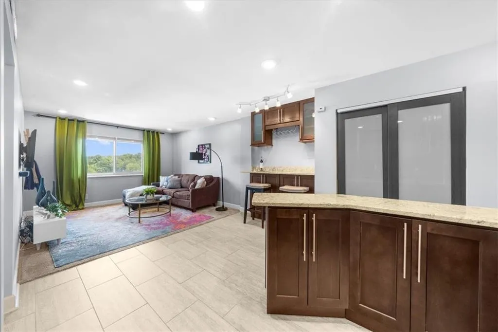 Kitchen featuring recessed lighting, glass insert cabinets, light stone counters, light tile patterned floors, and dark brown cabinets