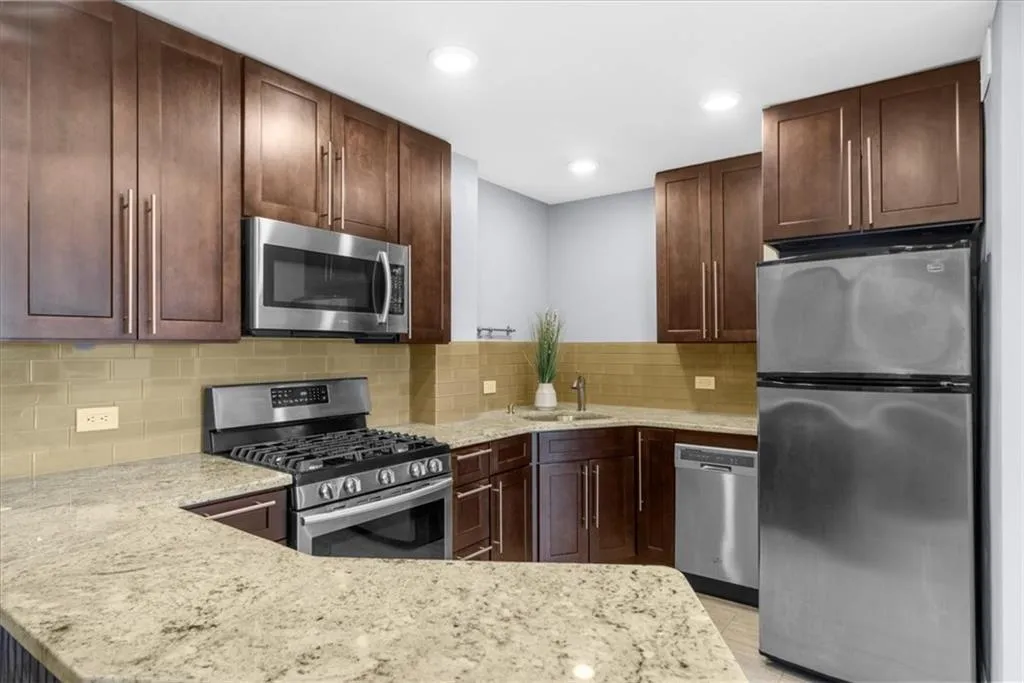Kitchen with appliances with stainless steel finishes, decorative backsplash, recessed lighting, light stone counters, and a peninsula