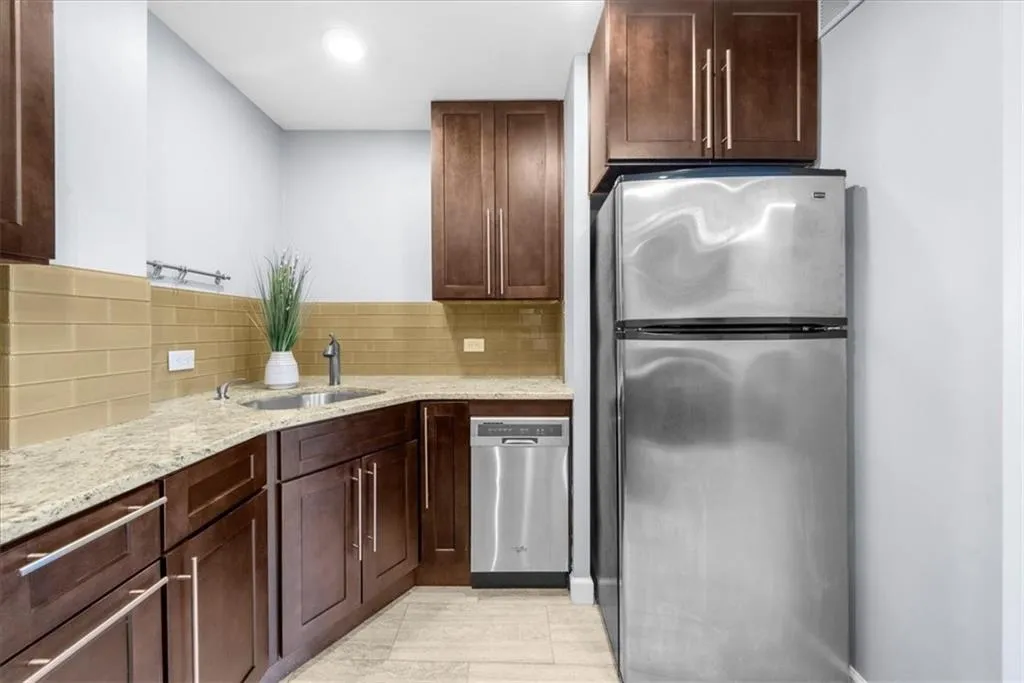 Kitchen featuring appliances with stainless steel finishes, light stone countertops, and backsplash
