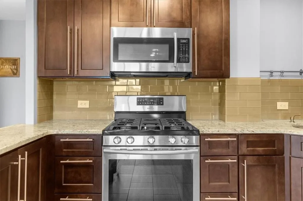 Kitchen featuring stainless steel appliances, decorative backsplash, and light stone counters