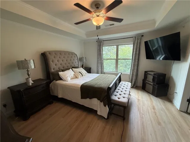 Bedroom featuring wood-finish flooring, a tray ceiling with crown molding, and a ceiling fan