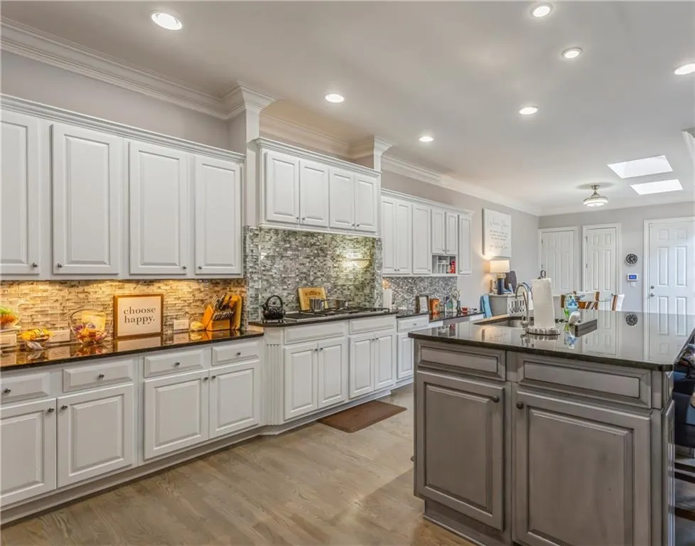 Kitchen featuring ornamental molding, a skylight, white cabinets, dark stone counters, and tasteful backsplash