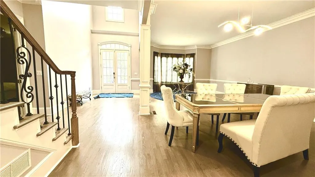 Dining area with crown molding, stairs, wood finished floors, ornate columns, and french doors