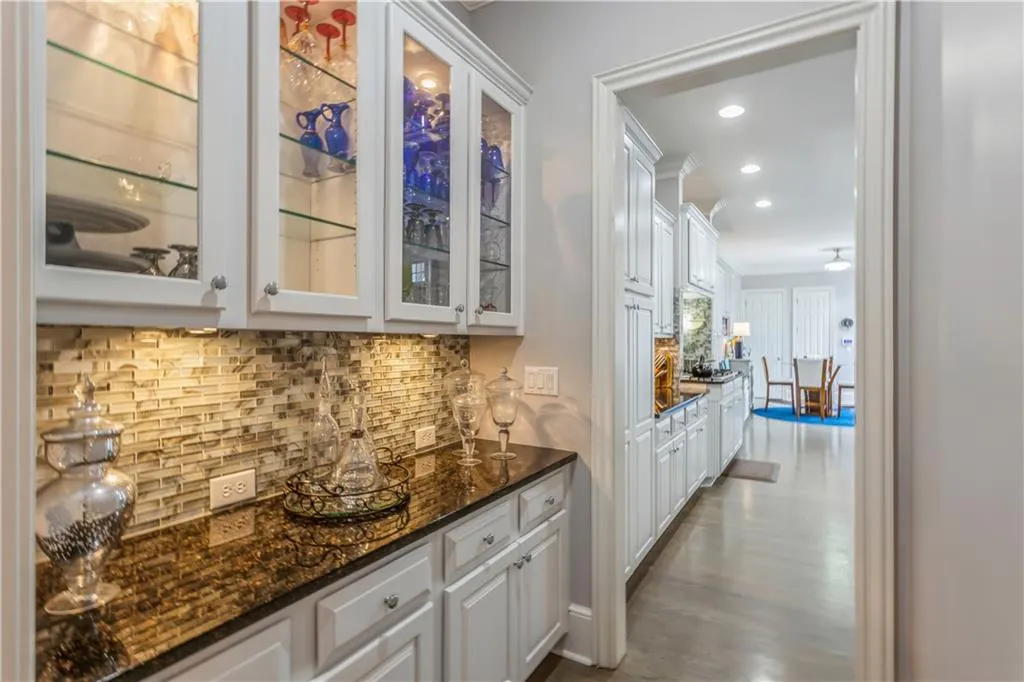 Bar area with backsplash, white cabinets, glass insert cabinets, dark stone counters, and recessed lighting