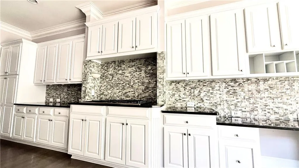 Kitchen with decorative backsplash, white cabinets, ornamental molding, open shelves, and dark stone countertops