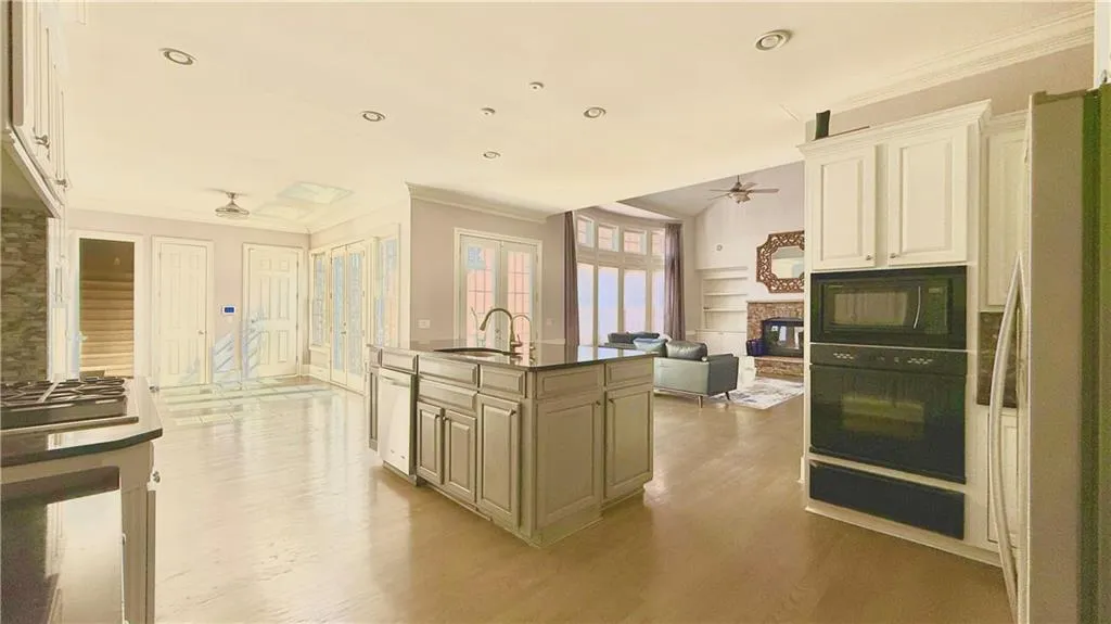 Kitchen with crown molding, black appliances, a glass covered fireplace, ceiling fan, and cream cabinetry