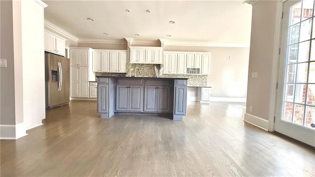 Kitchen with backsplash, stainless steel fridge, a kitchen island with sink, crown molding, and white cabinets
