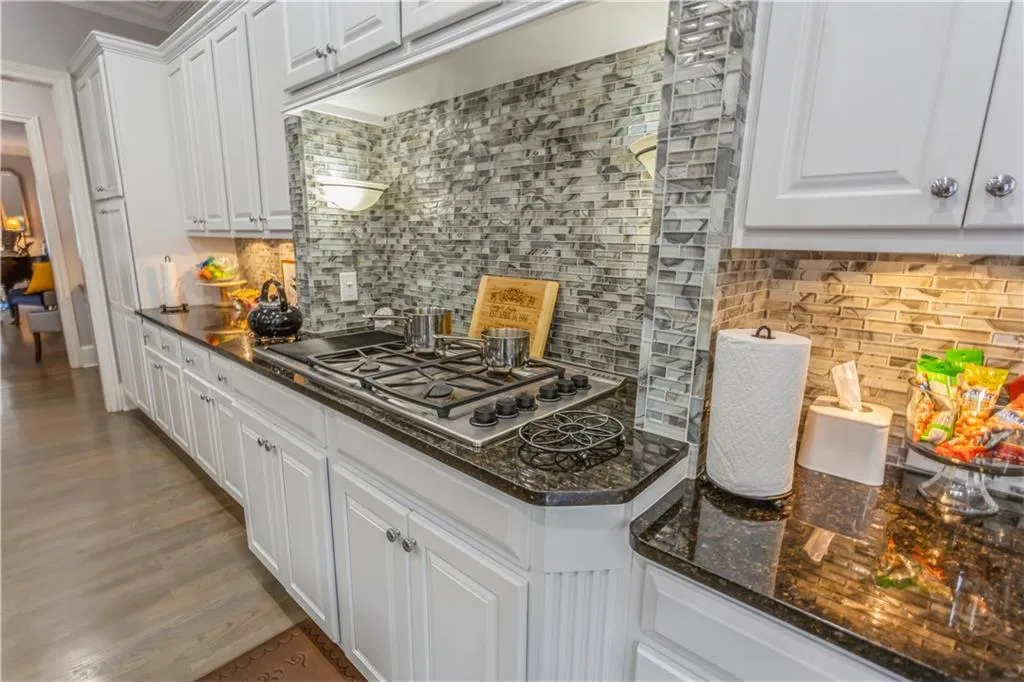 Kitchen featuring tasteful backsplash, white cabinetry, dark stone countertops, stainless steel gas cooktop, and light wood finished floors