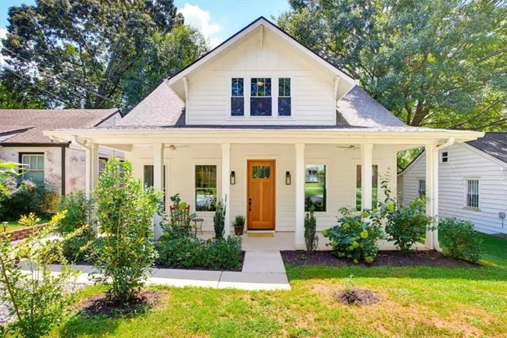 White-paneled exterior with a covered front porch, natural wood entry door, and a gabled roofline