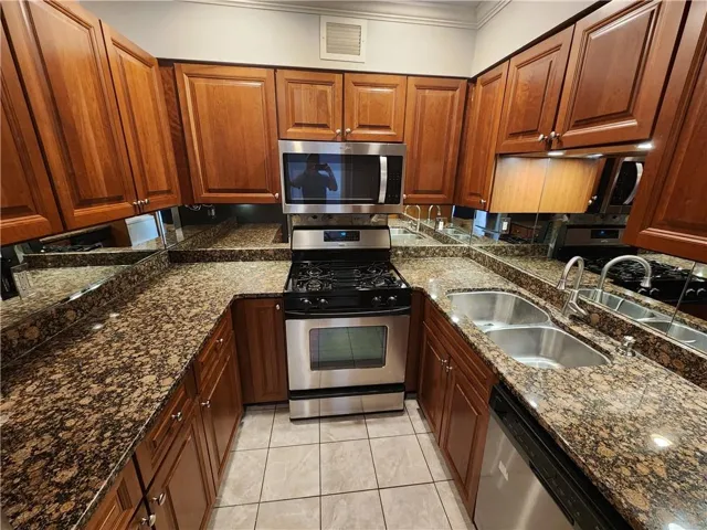 Kitchen with stainless steel appliances, sink, light tile patterned floors, crown molding, and dark stone countertops