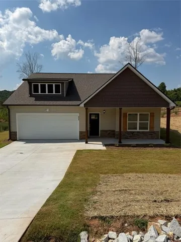 Single-story residence featuring a two-car garage, dormer window with multiple panes, stone veneer accents, and a covered front porch with wood columns