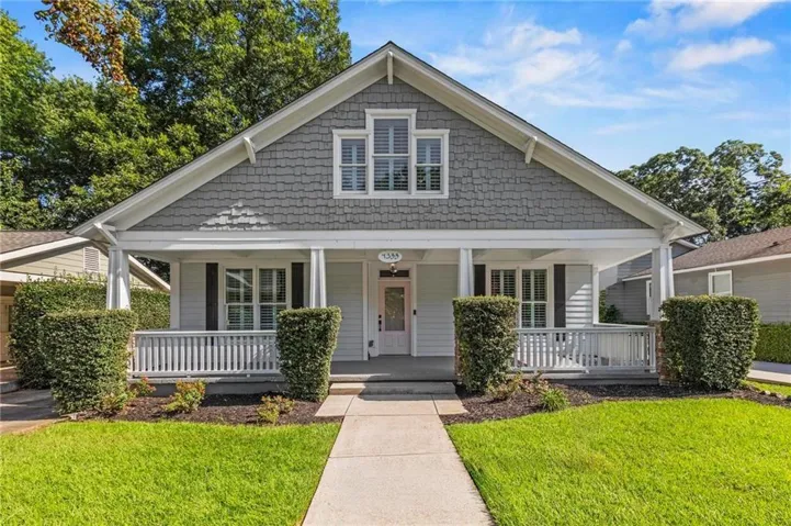 Gable roofline, shingle siding, covered front porch, white balustrade, and mature landscaping