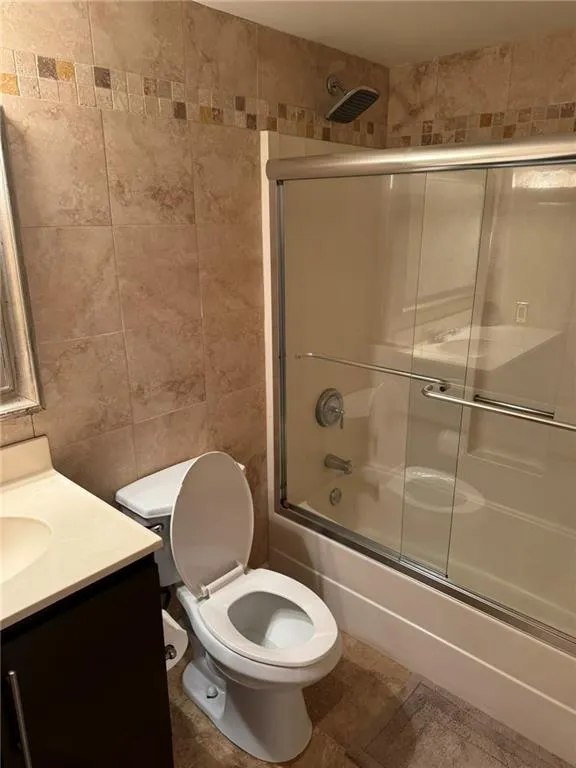 Full bath with tile shower walls, vanity, and bath/shower combo with glass door