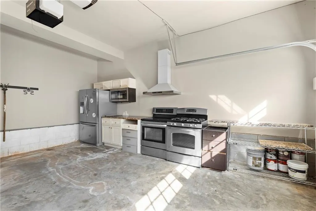 Kitchen with appliances with stainless steel finishes, unfinished concrete floors, and wall chimney range hood