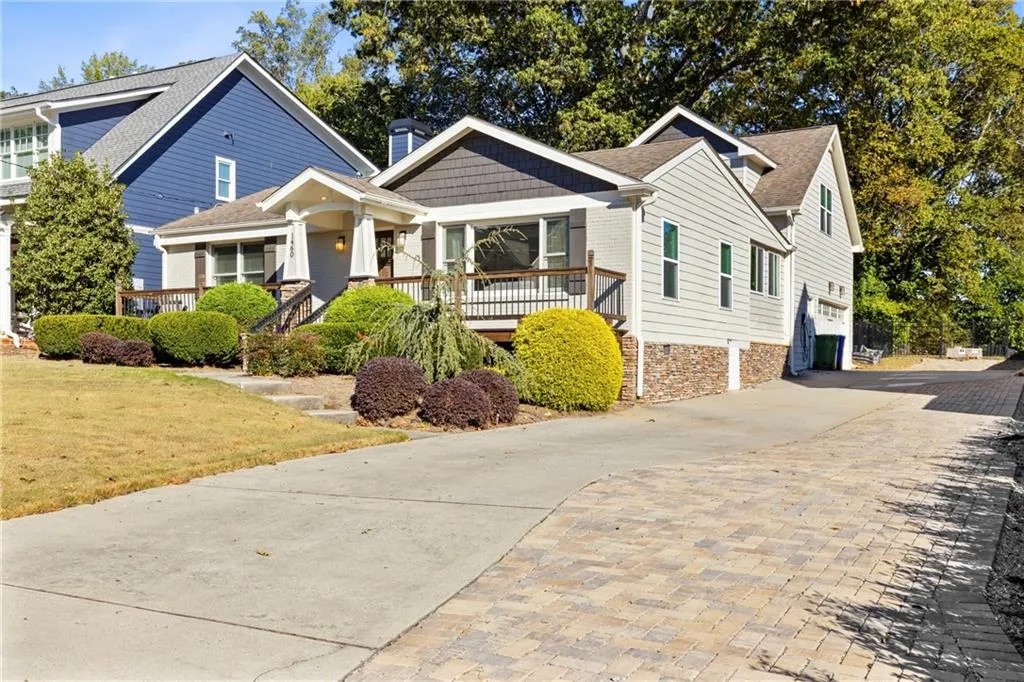 Craftsman-style house with decorative driveway, a chimney, roof with shingles, a porch, and a front lawn
