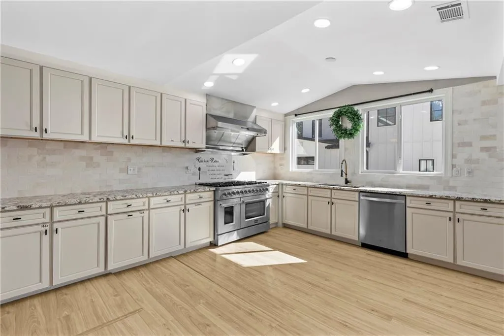 Kitchen featuring stainless steel appliances, tasteful backsplash, light stone counters, light wood-style flooring, and vaulted ceiling