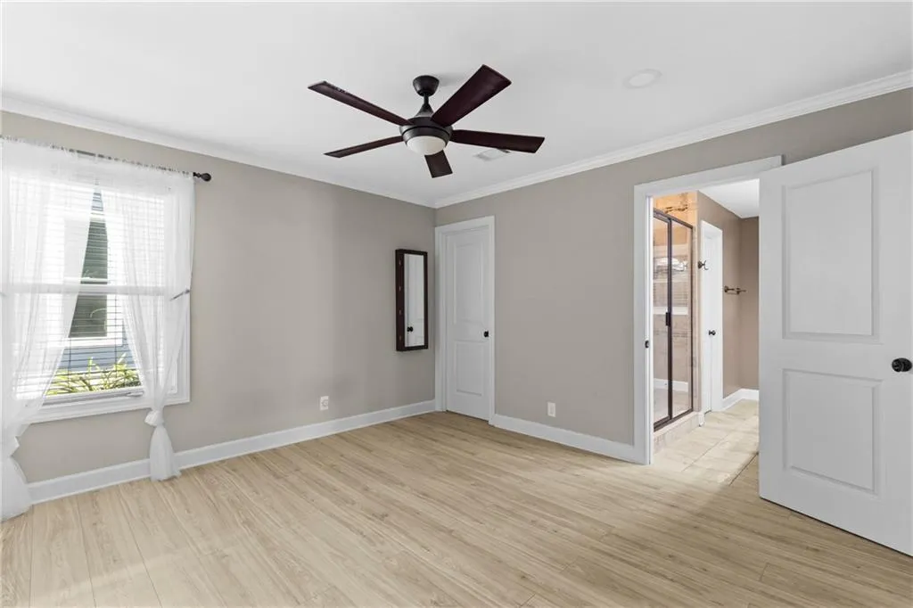 Unfurnished bedroom featuring ornamental molding, light wood-style flooring, a ceiling fan, and ensuite bathroom