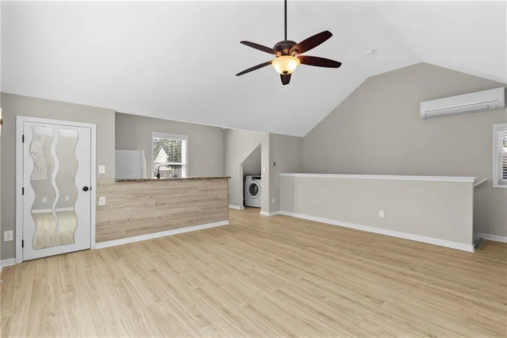 Unfurnished living room featuring light wood finished floors, vaulted ceiling, a ceiling fan, an AC wall unit, and washer / clothes dryer