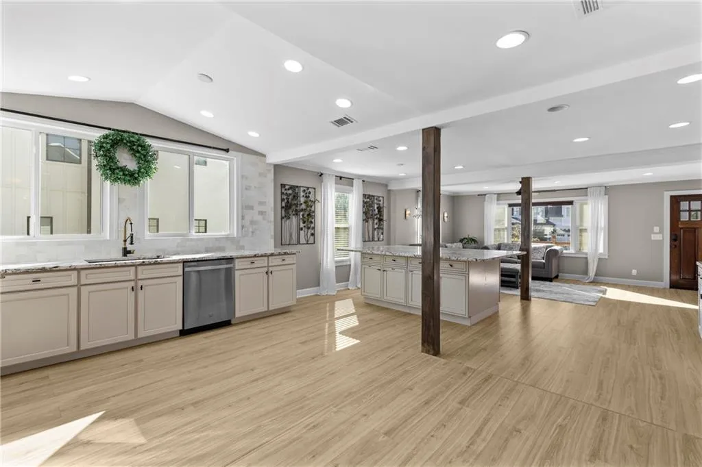 Kitchen featuring open floor plan, light wood-style floors, decorative backsplash, stainless steel dishwasher, and light stone counters