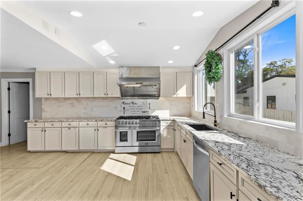 Kitchen with appliances with stainless steel finishes, recessed lighting, tasteful backsplash, light wood-style flooring, and light stone countertops
