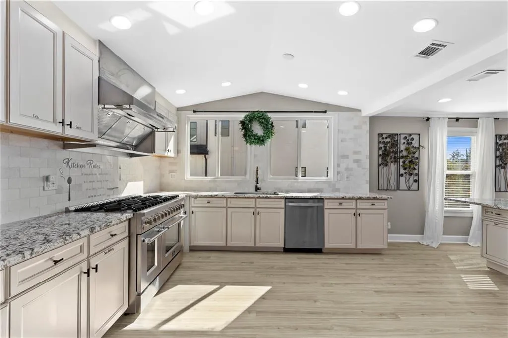 Kitchen featuring decorative backsplash, appliances with stainless steel finishes, light stone counters, lofted ceiling, and recessed lighting