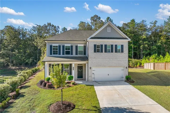 Two-story exterior with a covered porch, brick and siding facade, attached two-car garage, and concrete driveway