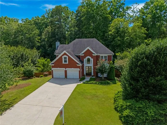 Traditional brick exterior with an arched entryway, twin garage doors, a concrete driveway, and established perimeter landscaping