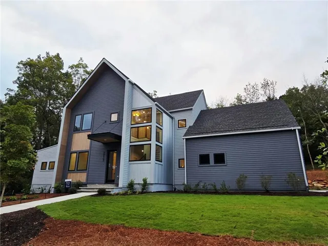 Modern architectural exterior featuring multiple siding textures, a prominent gabled roofline, a stepped entry, and a multi-story window installation