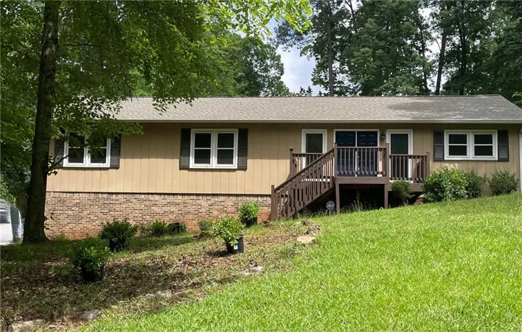 Split-level residence featuring a wood deck with stairs, brick foundation, and light-colored siding