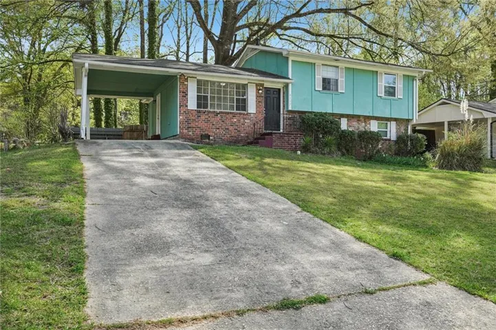 Split-level residence featuring a brick and mint green facade, a covered carport, and an extended concrete driveway