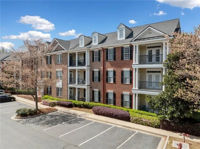 #303 is on the 3rd floor corner unit on the  BACKSIDE of building overlooking the trees. Brick exterior with multiple balconies and dormer windows, featuring established landscaping and an asphalt parking area