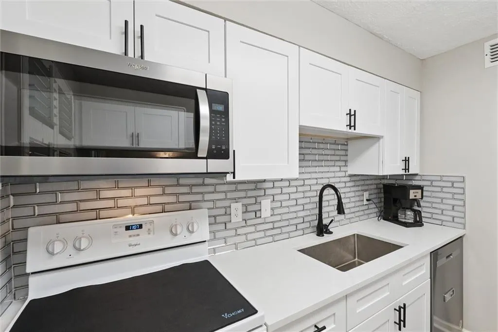 Kitchen featuring stainless steel appliances, white cabinetry, tasteful backsplash, a textured ceiling, and light stone countertops