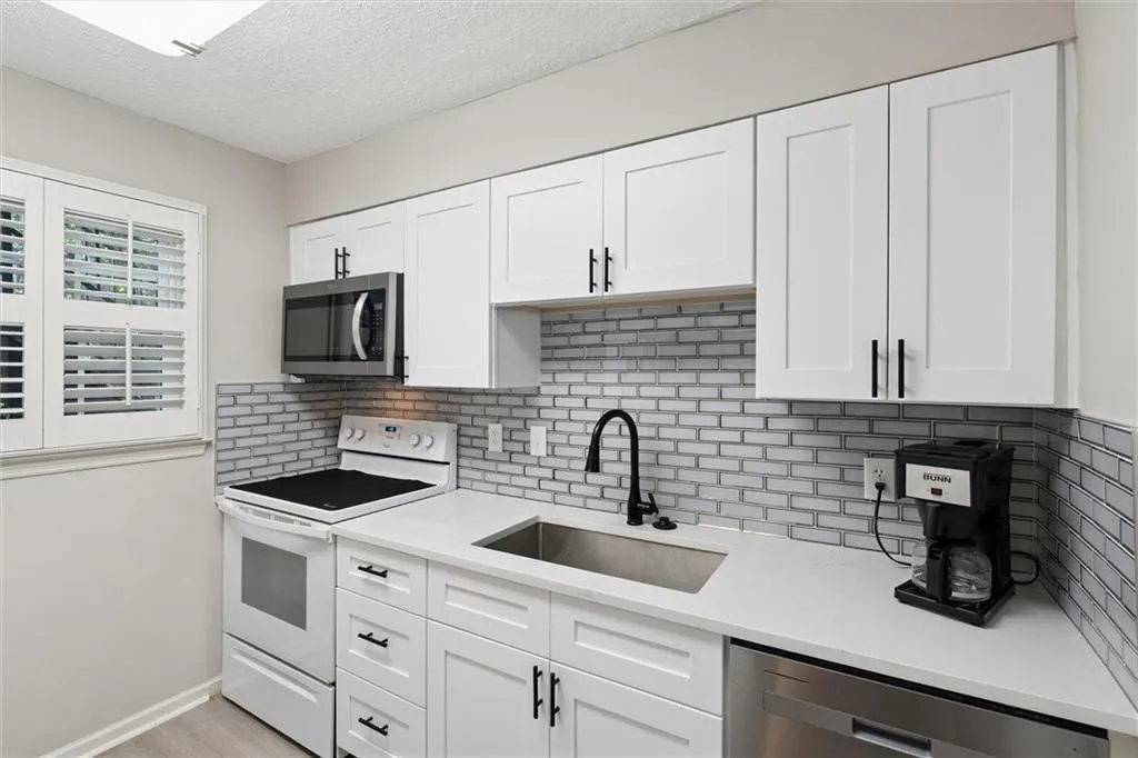 Kitchen featuring appliances with stainless steel finishes, white cabinetry, decorative backsplash, a textured ceiling, and light stone countertops