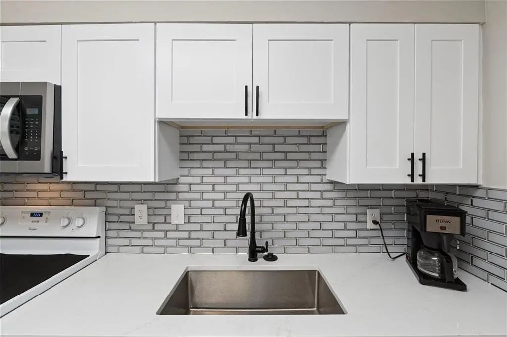 Kitchen featuring backsplash, white range oven, white cabinetry, stainless steel microwave, and light stone countertops