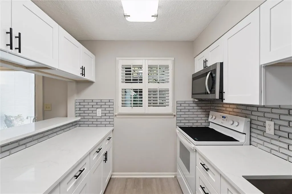 Kitchen with electric stove, white cabinetry, light stone counters, backsplash, and a textured ceiling