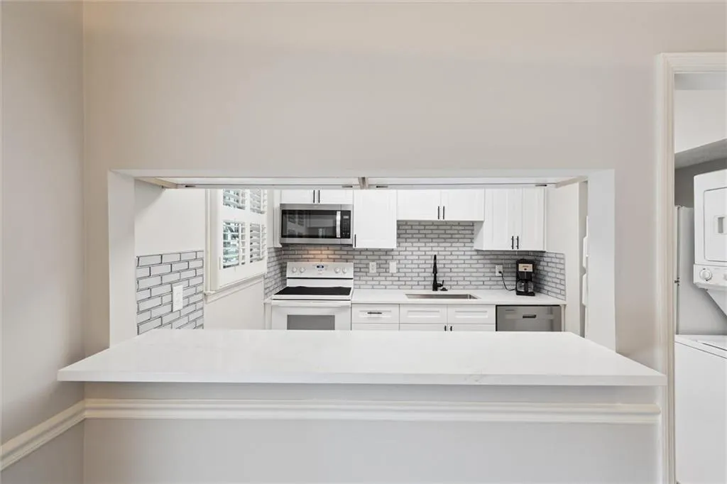 Kitchen with white cabinets, stainless steel appliances, light stone countertops, tasteful backsplash, and stacked washer and clothes dryer
