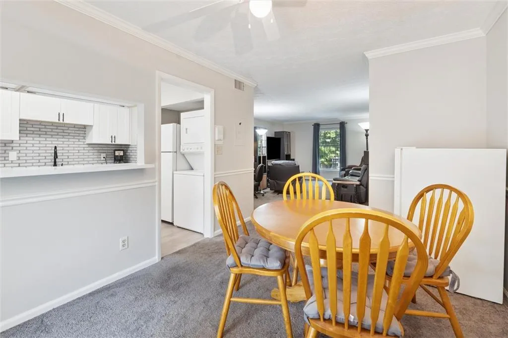 Dining area with ornamental molding, stacked washer / drying machine, light colored carpet, and ceiling fan