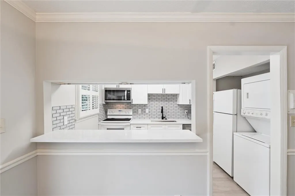 Kitchen featuring white cabinets, crown molding, backsplash, white appliances, and stacked washer / drying machine