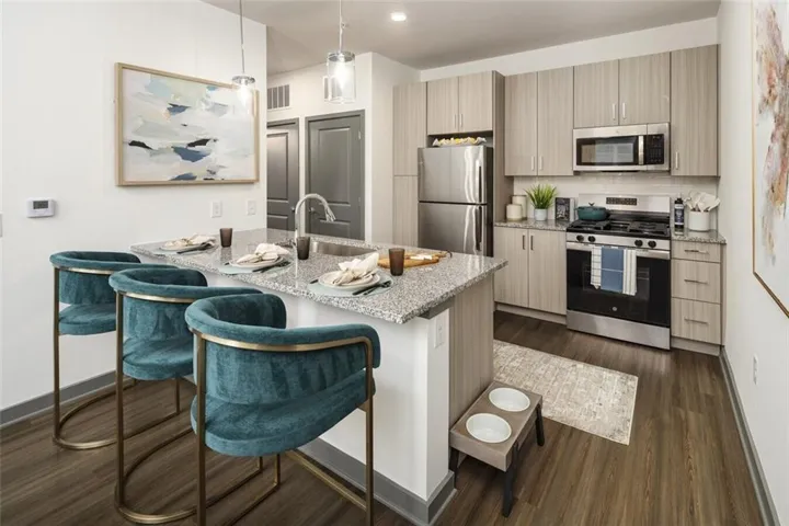 Kitchen featuring appliances with stainless steel finishes, light stone counters, a peninsula, pendant lighting, and a breakfast bar