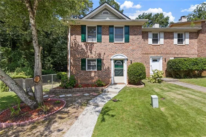 Welcoming brick Colonial with manicured lawn, mature landscaping, and established shade trees