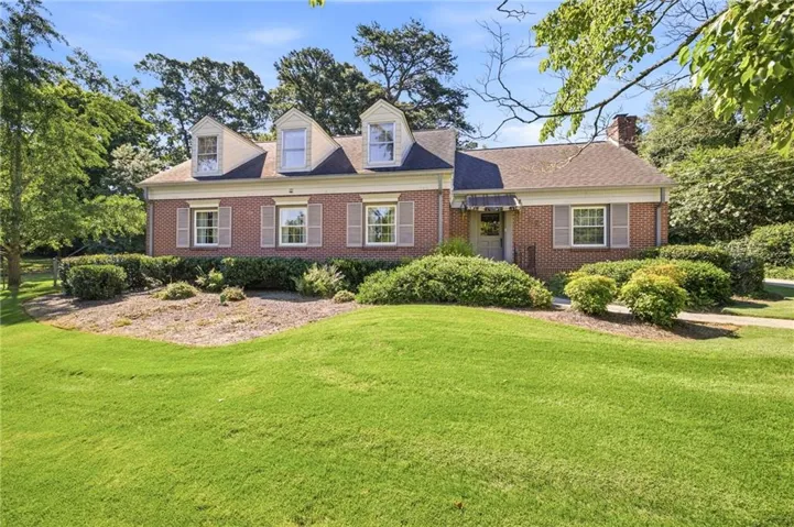 Traditional brick facade residence featuring a front lawn, mature landscaping, three dormer windows, and a covered entry