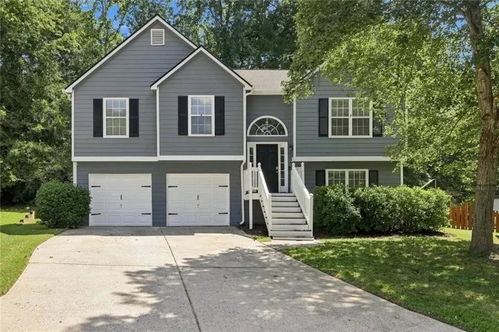 Split-level exterior featuring gray siding, a two-car garage, white railings, and a prominent arched transom window