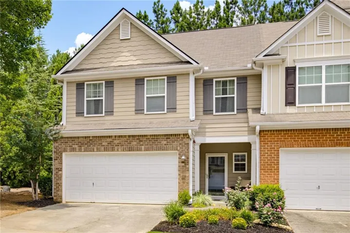 Multi-level townhome exterior featuring light-colored siding, brick accent details, and a two-car garage