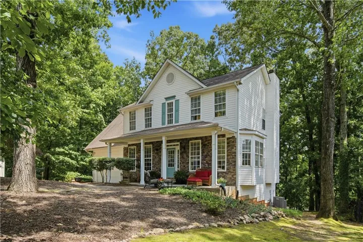 Two-story residence featuring a covered front porch, stone and siding exterior, bay window, and a prominent gable with a circular accent