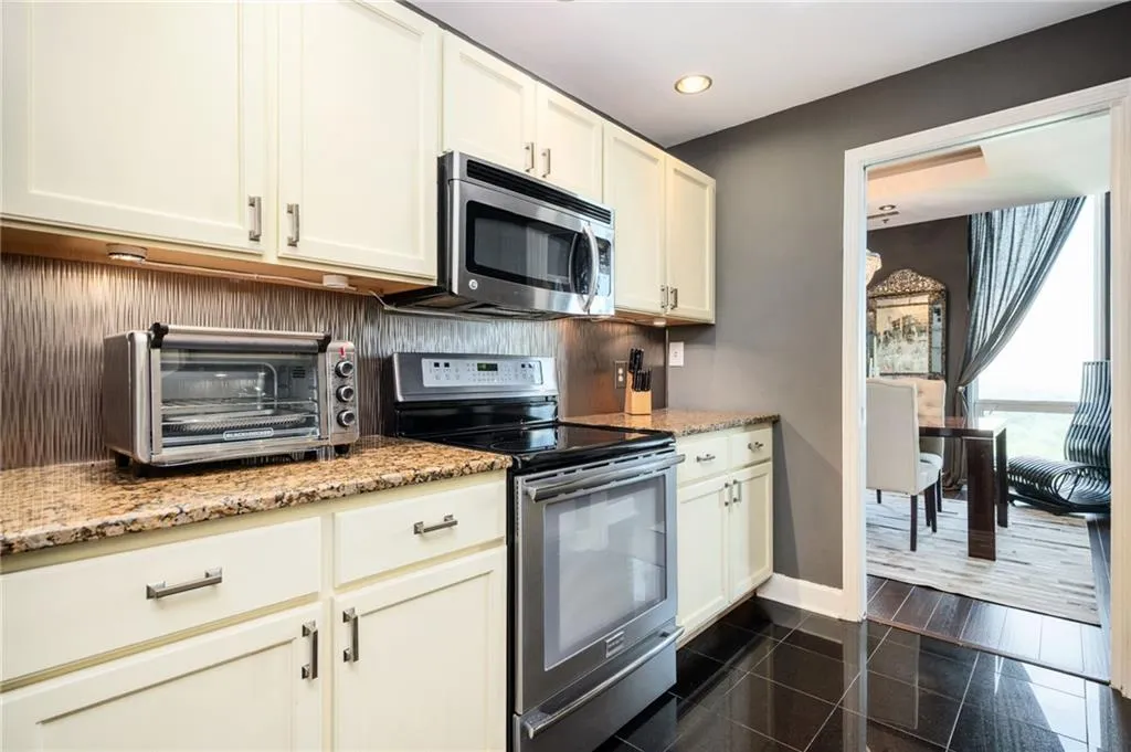 Kitchen with appliances with stainless steel finishes, recessed lighting, granite floors, light stone counters, and white cabinets